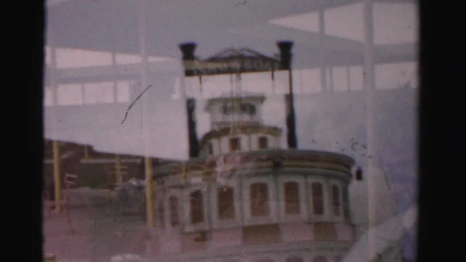 1957 Las Vegas frame showing a decorative paddlewheel-style riverboat facade near the resort pool deck, with distant people and structural shadows.