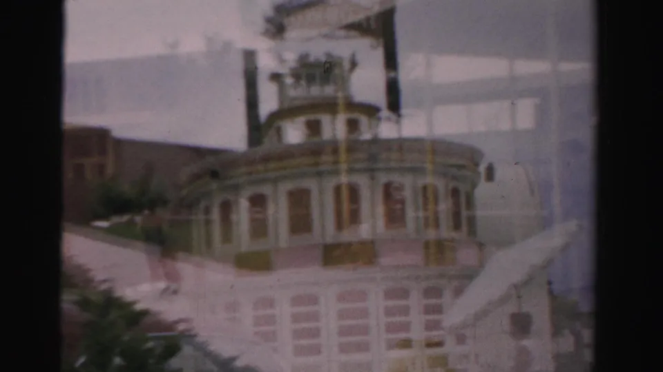 1957 Las Vegas home-movie frame with a soft cross-fade over a riverboat-like resort facade, exterior stairs, and visible film gate edges.