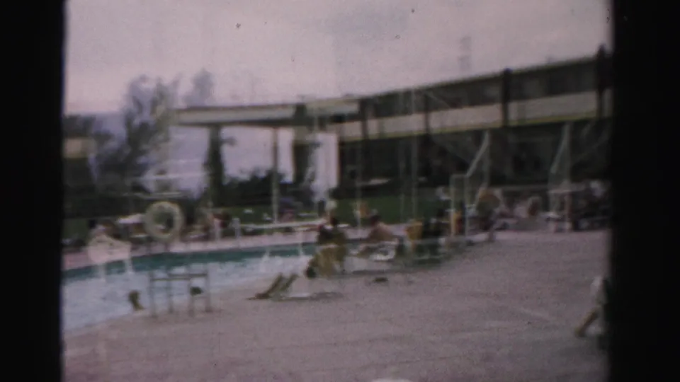 1957 Las Vegas resort pool scene with swimmers, lounge chairs, deck furniture, trees, and background structures on 8mm film.