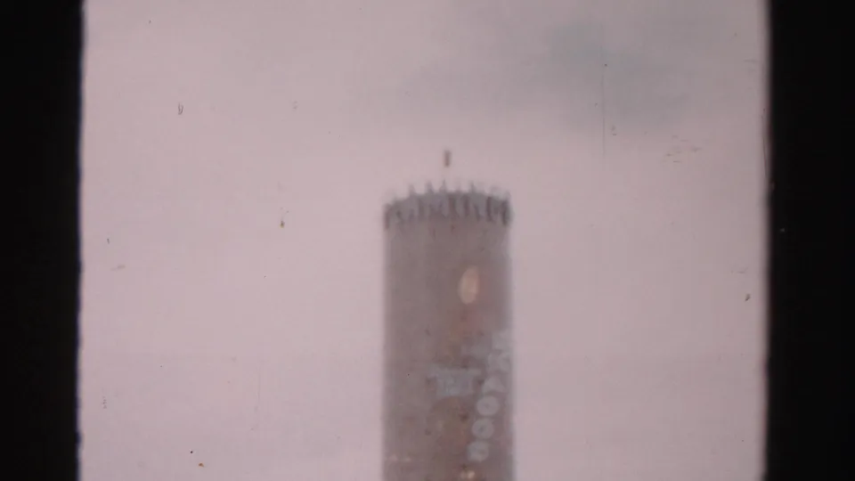 Low-angle 1957 Las Vegas home-movie view of the cylindrical tower, with soft focus, pale sky, and visible lettering on the structure.