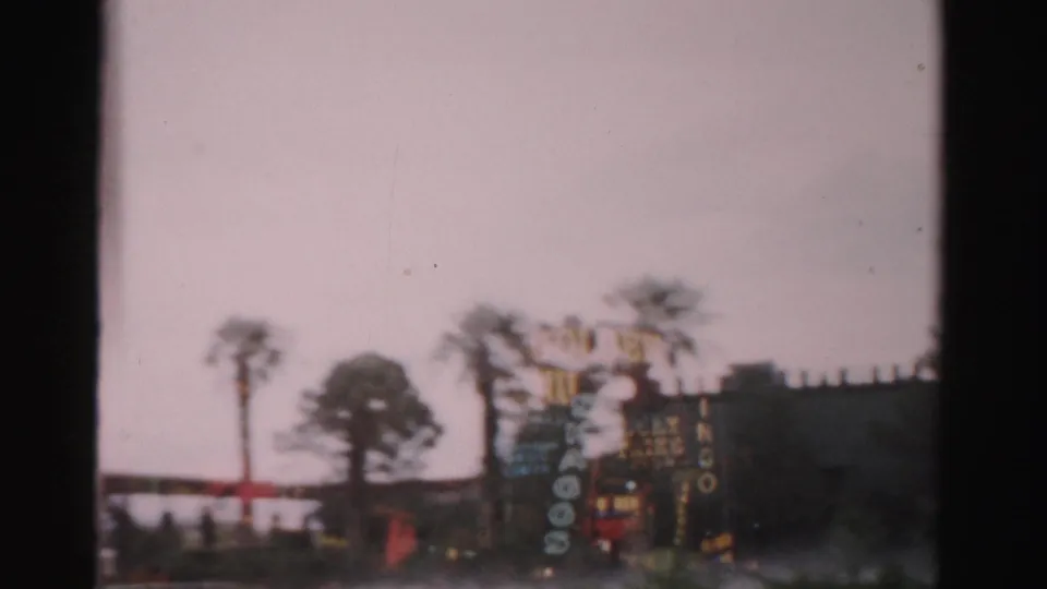 1957 Las Vegas frame with the Hotel Flamingo sign partly visible beside palm trees and dark window framing.