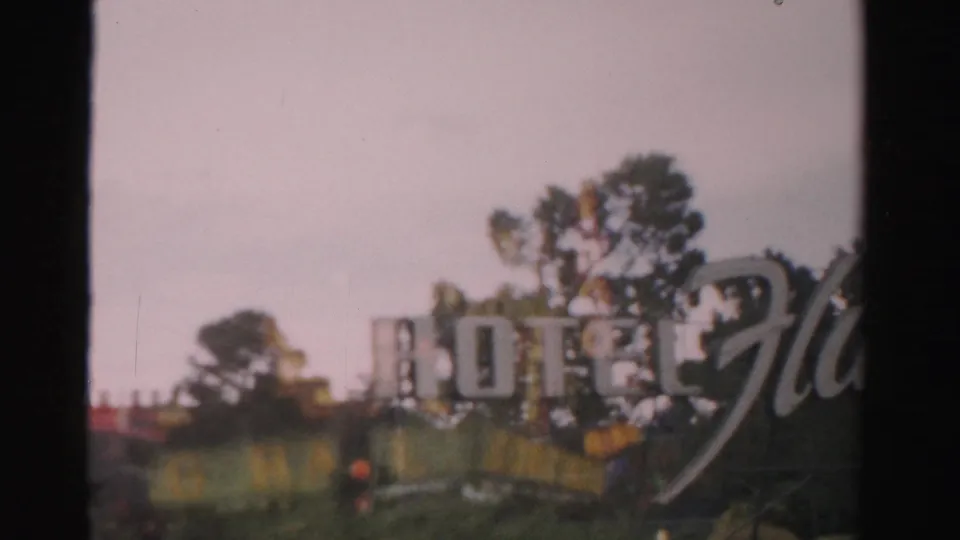 1957 Las Vegas frame with large hotel lettering, trees, partial signage, and soft 8mm color through a framed view.