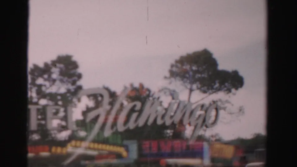 1957 Las Vegas home-movie frame showing the Flamingo sign, colorful resort frontage, trees, and a dark vertical frame edge.