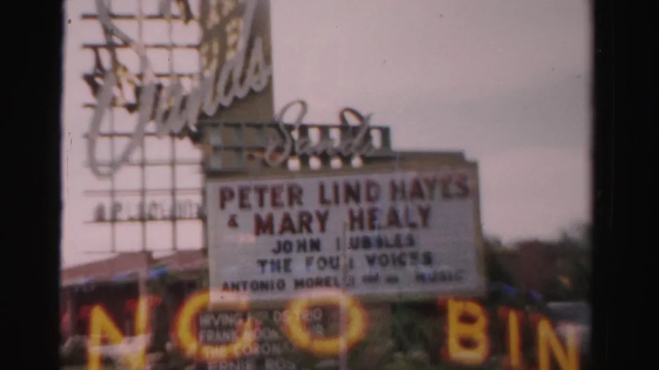 1957 Las Vegas home-movie frame with the Sands marquee, performer names, and blurred foreground neon or signage along the bottom edge.