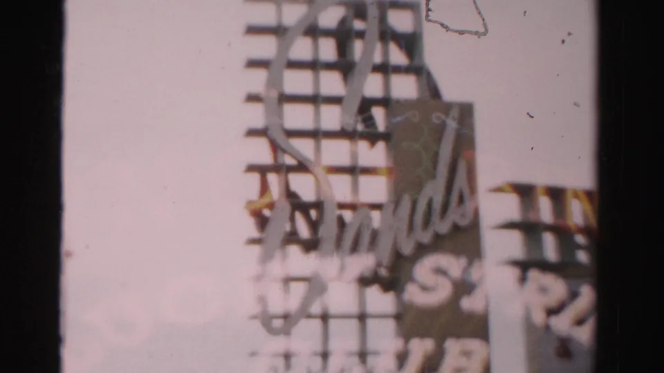 1957 Las Vegas frame showing a partial close view of the Sands sign, neon tubes, and metal sign framework against the sky.