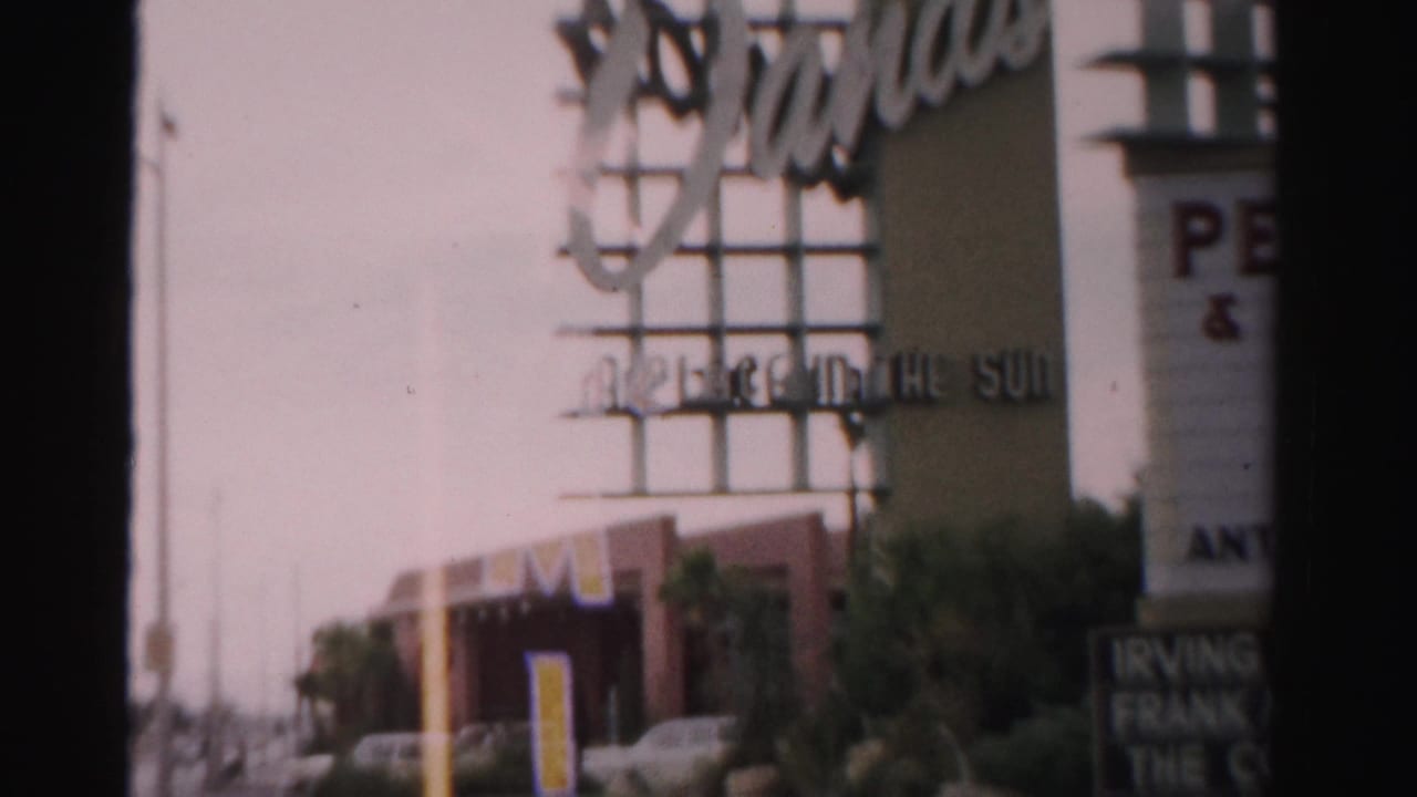 Commercial building with signage, palm landscaping, and parked cars along the street.