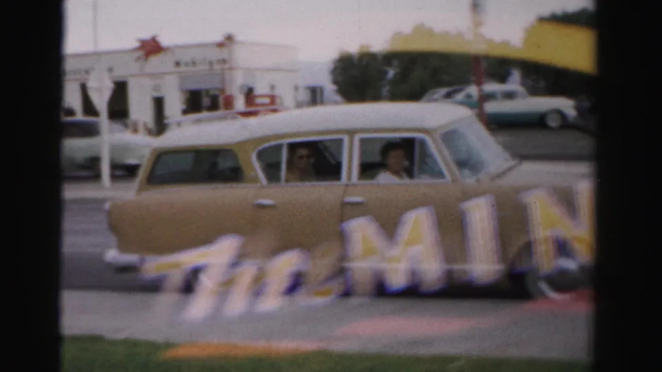 A beige station wagon passes in Las Vegas with The Mint lettering in the foreground and a Mobilgas station across the street.