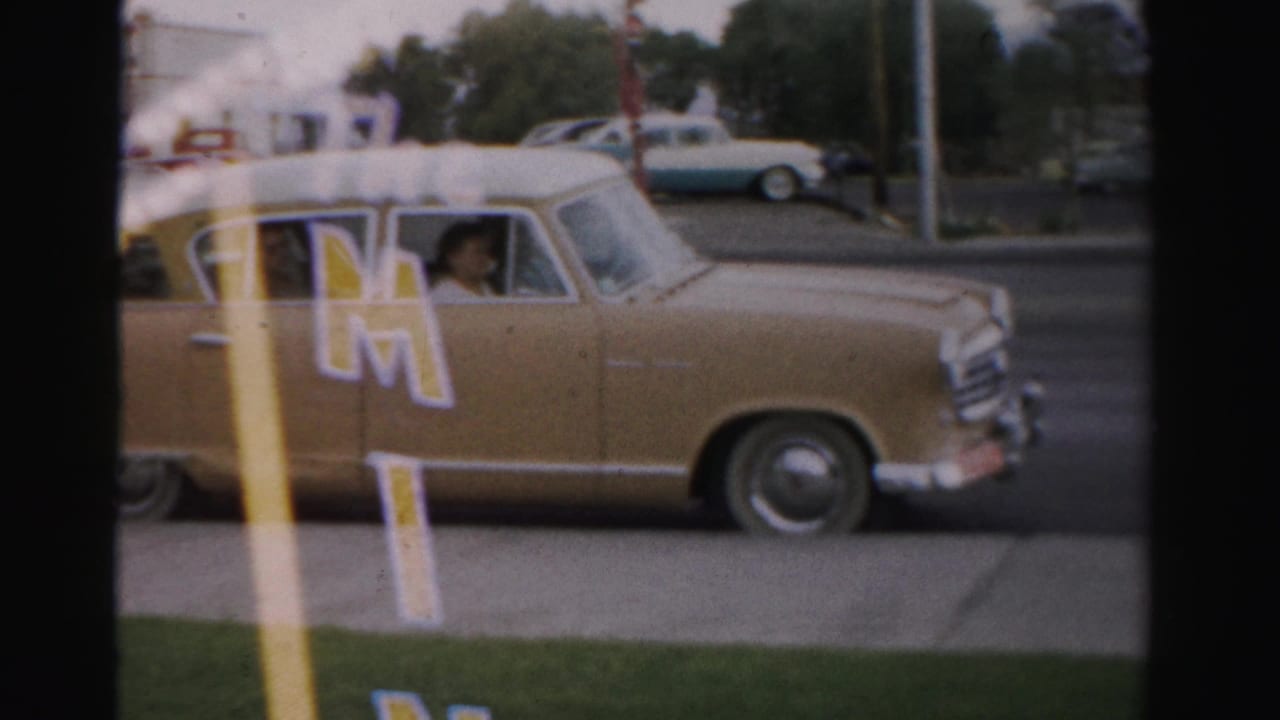 1957 Las Vegas street frame with a tan station wagon, white roof, The Mint lettering, grass verge, and a visible passenger face.