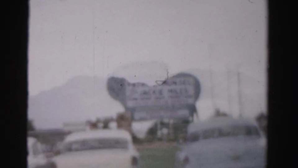 Soft 1957 Las Vegas street view showing pale classic cars, a large Jackie Miles sign, and hazy roadway detail.