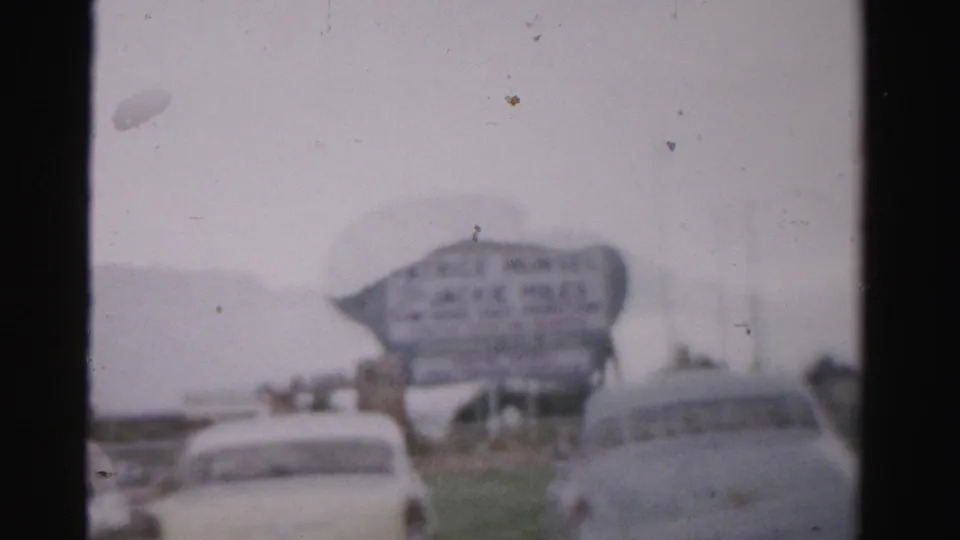 1957 Las Vegas frame with blurred classic cars, a large Jackie Miles sign, grass, roadway, and soft home-movie color.