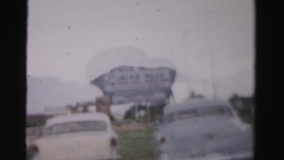 Soft 1957 Las Vegas street frame with pale cars, a large Jackie Miles sign, roadway, grass, and visible 8mm texture.