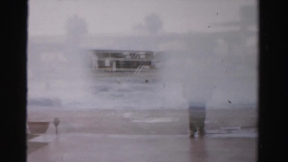 A hazier frame shows the man partly obscured by exposure and film softness, with wet shoreline and a distant low structure visible.