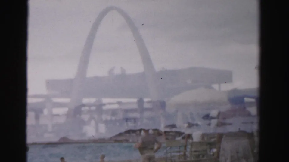 Layered 8mm frame from 1957 Las Vegas showing a pool, swimmers, umbrellas, and a large arch-shaped structure softened by haze and double exposure.