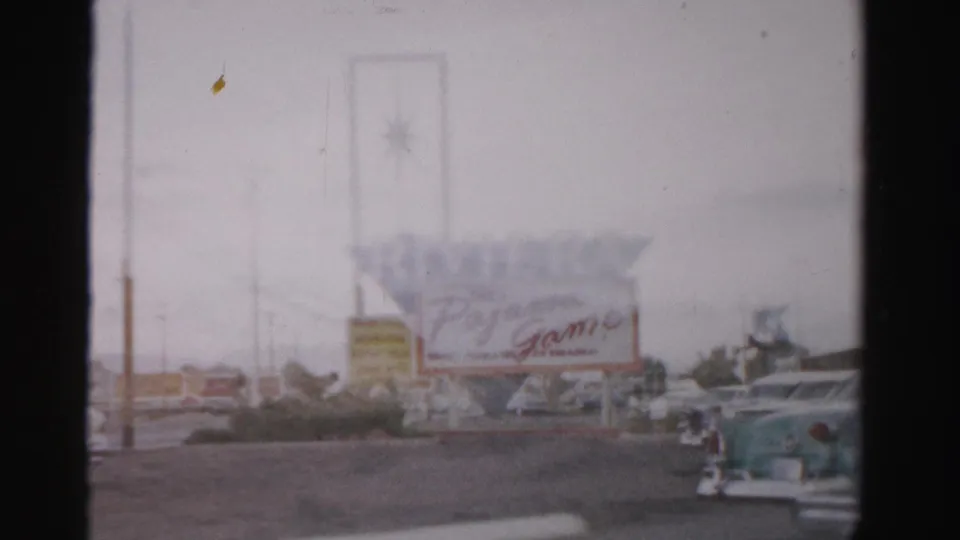 1957 Las Vegas view of the Riviera sign and Pajama Game marquee, with classic cars and a roadside commercial strip visible through soft focus.