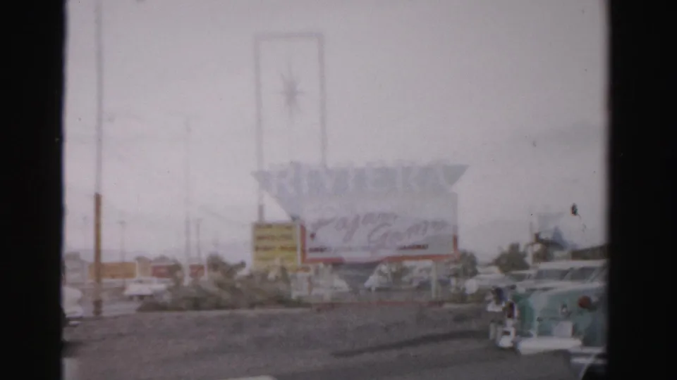 1957 Las Vegas frame with the Riviera sign and Pajama Game marquee receding behind a street edge and a turquoise mid-century car.