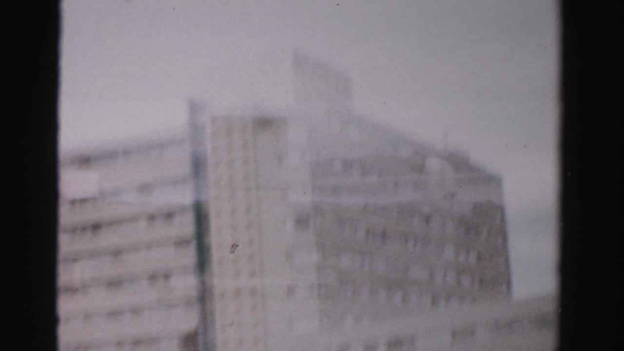 1957 Las Vegas frame with a multi-story building facade and roadside structures partially obscured by a dark vertical divider.