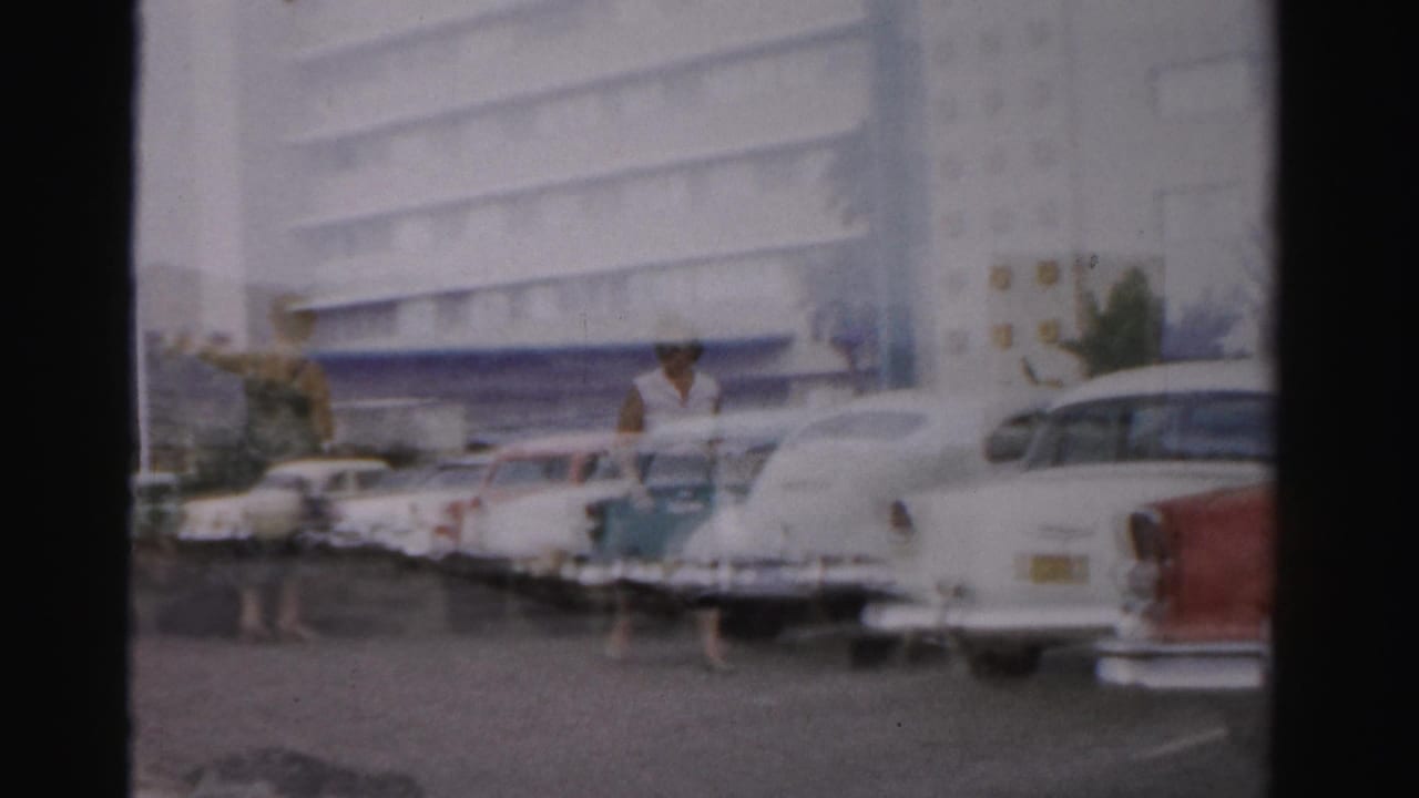 Parked 1950s cars line a Las Vegas parking lot as a person walks past a large building.