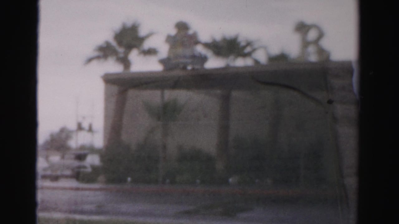 1957 Las Vegas home-movie frame showing a soft, distant view of the Royal Nevada area with rooftop decoration, palms, and street frontage.