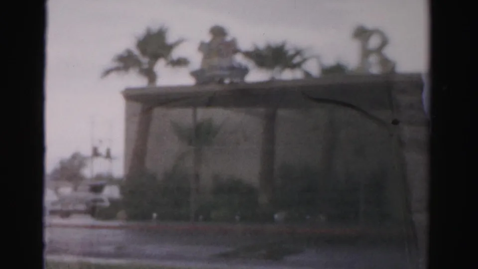 1957 Las Vegas home-movie frame showing a soft, distant view of the Royal Nevada area with rooftop decoration, palms, and street frontage.