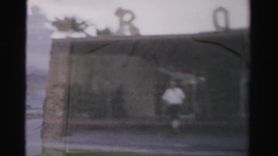 1957 Las Vegas home-movie frame with a blurred passerby near the Royal Nevada building frontage and rooftop decorative forms.