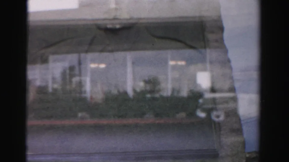 Faded 1957 Las Vegas home-movie frame showing windows, landscaping, curb line, and a parked car near the Royal Nevada frontage.