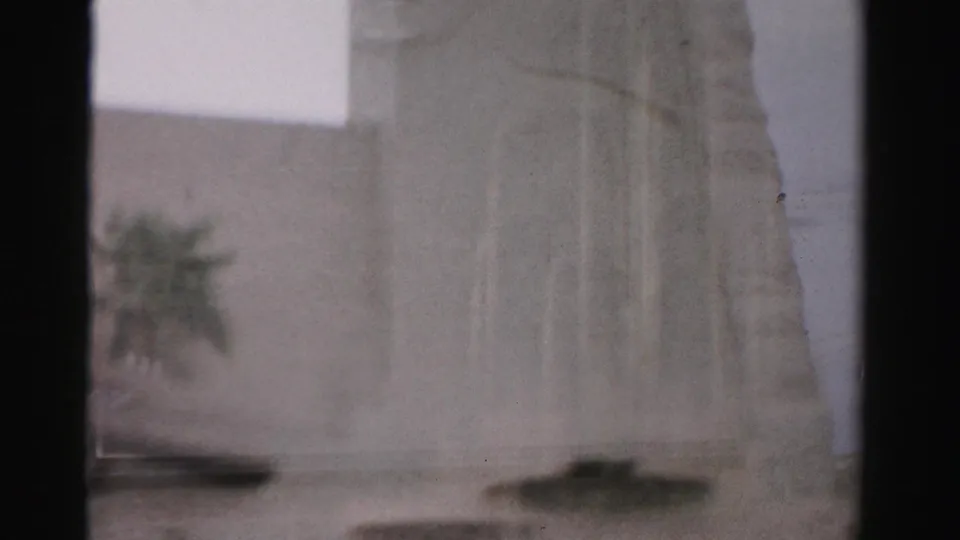 1957 Las Vegas home-movie frame looking through interior window bars at a pale exterior wall with soft focus and glare.