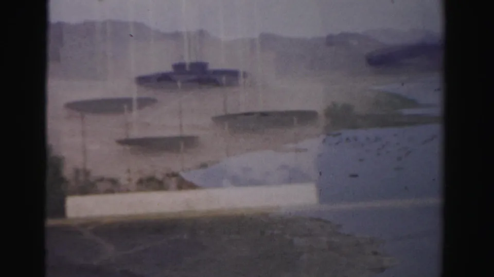 1957 Las Vegas home-movie view through window framing toward water, pale walls, low hills, and blurred architectural details.
