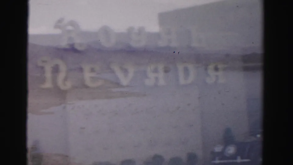 1957 Las Vegas 8mm frame with the Royal Nevada sign most visible, set over a soft desert lake view and a car at the edge.