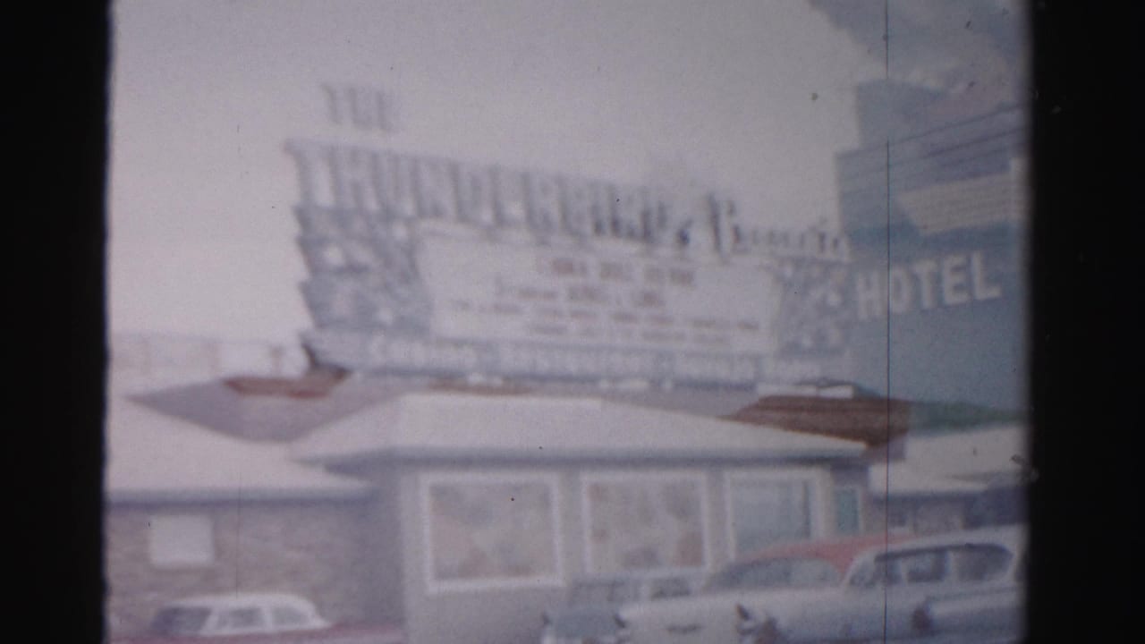 Soft 8mm frame of a roadside hotel exterior with marquee lettering and parked cars below.