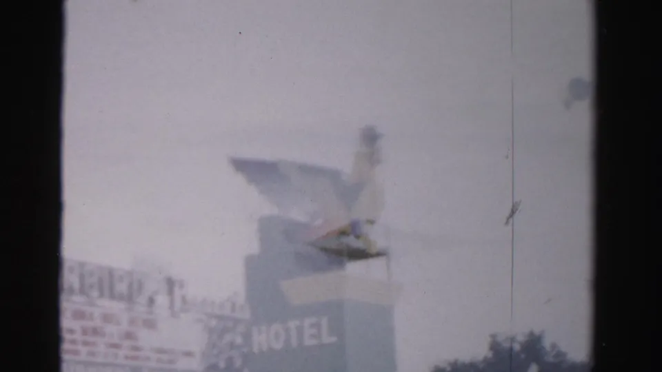1957 Las Vegas 8mm view of a hotel sign with large HOTEL letters and a giant bird mascot against a pale sky.