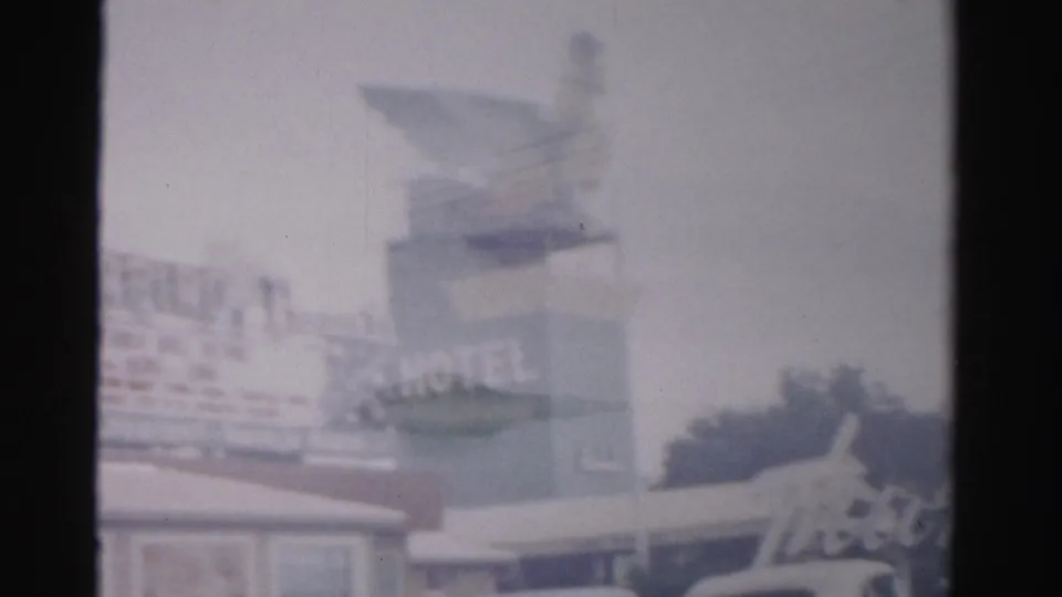 Soft 1957 Las Vegas home-movie frame with a partial hotel marquee, bird-topped sign, roofline, and trees.