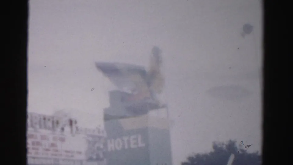 1957 Las Vegas 8mm frame showing the bird mascot above a hotel sign, with HOTEL lettering and trees below.