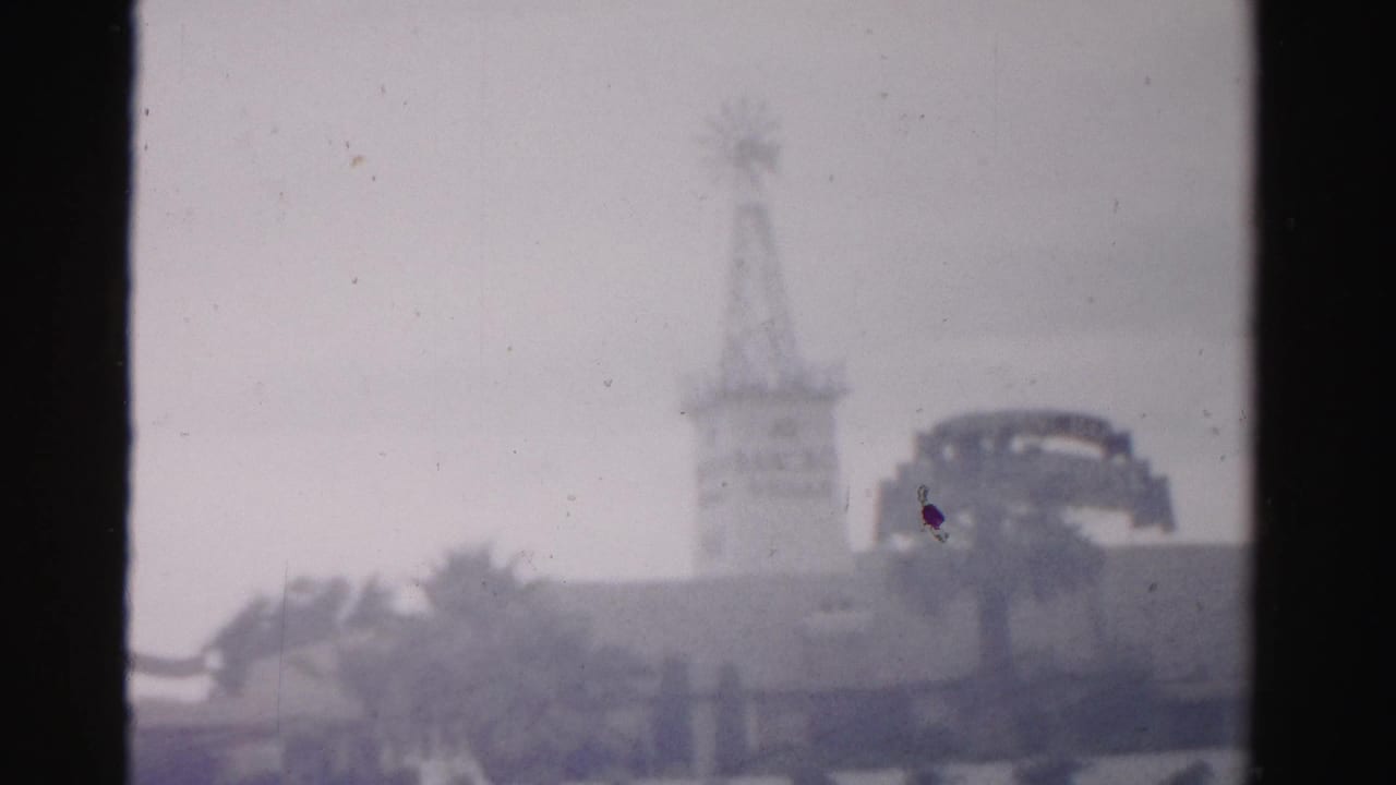 Windmill-style tower and palm trees with a dark rounded sign or structure at right.