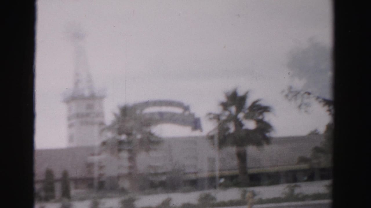 1957 Las Vegas frame with a soft-focus tower, arched sign-like form, palm tree, low building, and dark 8mm frame edge.