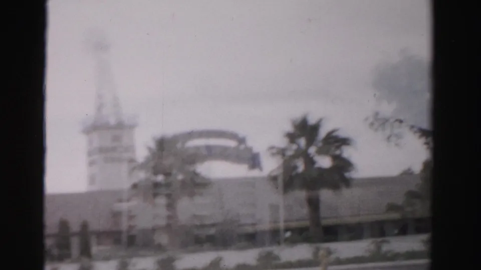 1957 Las Vegas frame with a soft-focus tower, arched sign-like form, palm tree, low building, and dark 8mm frame edge.