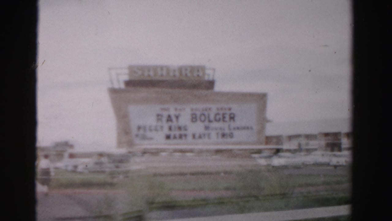 1957 Las Vegas frame with the Sahara Hotel marquee advertising Ray Bolger, with parked automobiles and hotel buildings behind it.