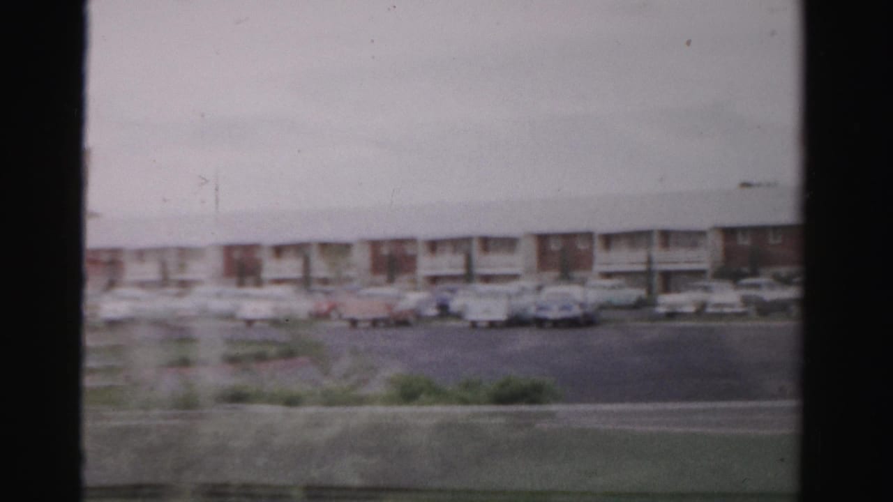 Long low motel building seen across a road with parked mid-century cars.