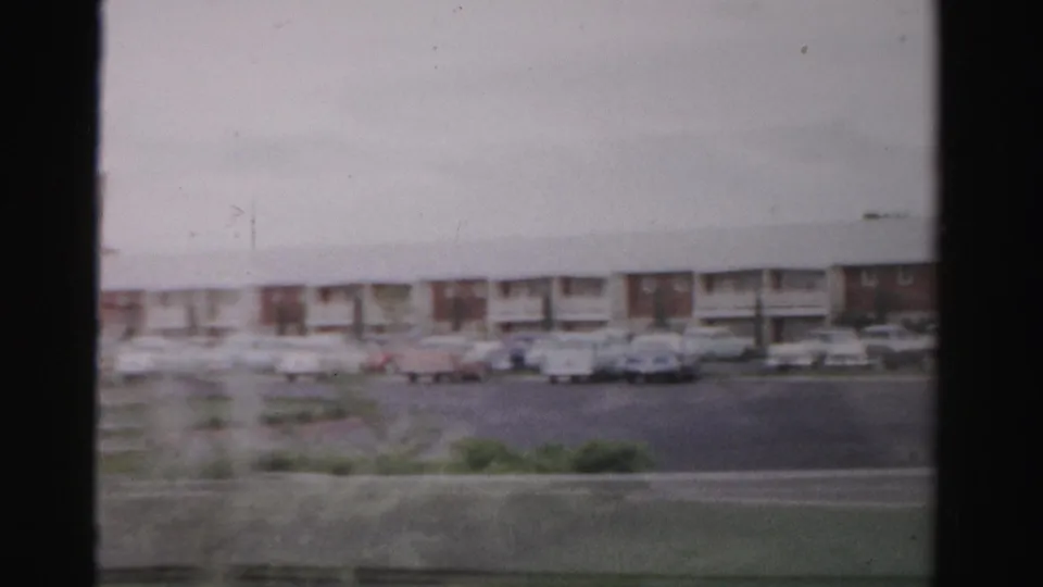 1957 Las Vegas home-movie frame showing a low motel frontage across a roadway with a parking lot and classic cars.