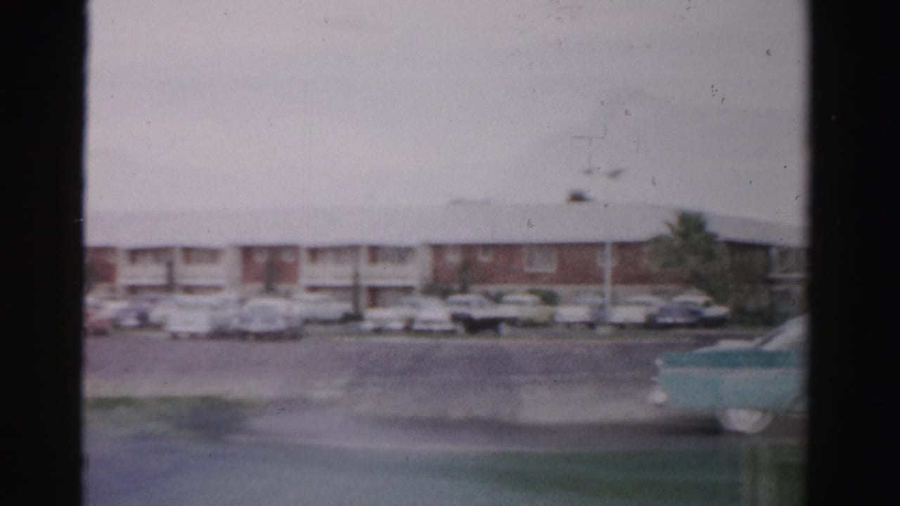 Motel parking lot and low building partly obscured by a turquoise vehicle in motion.