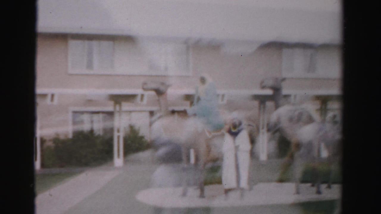 Two camel sculptures and several figures stand outside a beige building.