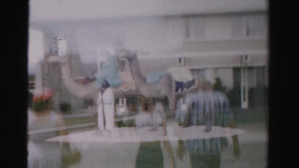 1957 Las Vegas frame with two camel sculptures, robe-like figures, and a beige building behind the display.
