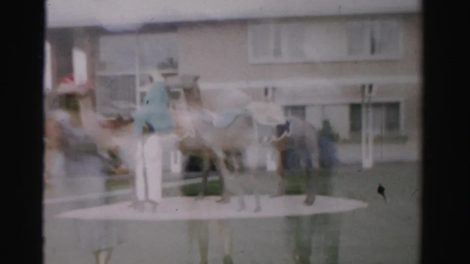Final soft 8mm frame of the Las Vegas camel display, with figures and a beige building facade in the background.
