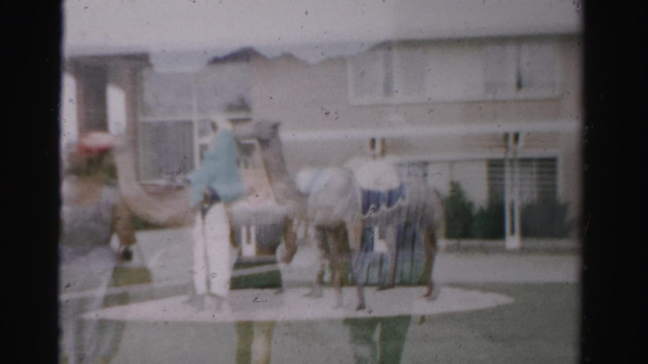 1957 Nevada home-movie frame showing a camel sculpture with riders near low suburban buildings, seen through soft 8mm focus.