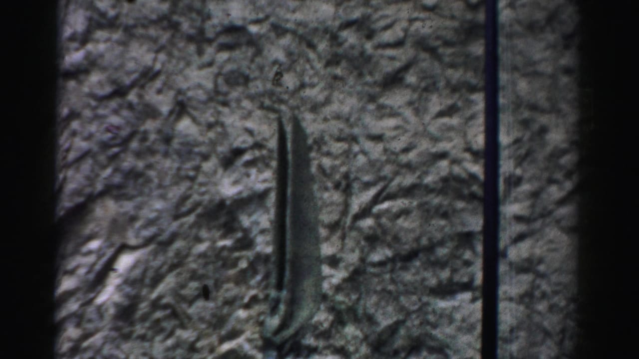 Close view of a rough stone wall with a vertical metal sculptural element.