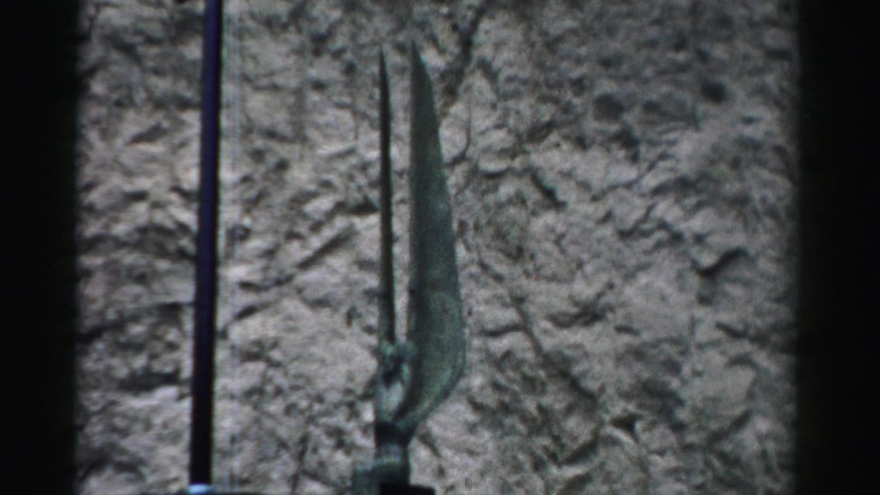 Tall green antenna-like forms stand in front of a textured rock face.