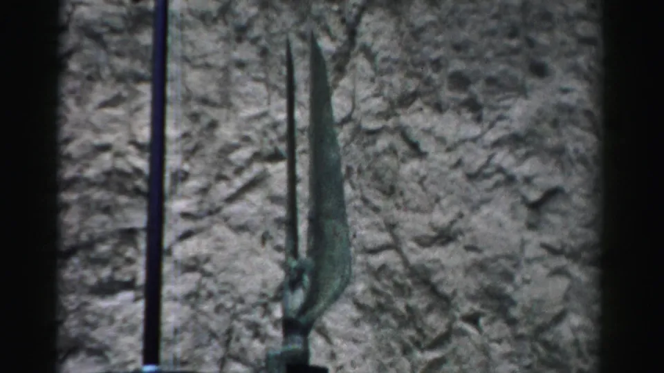 A distant 1957 Nevada view of tall curved antenna-like equipment set against a rugged stone or rock backdrop.