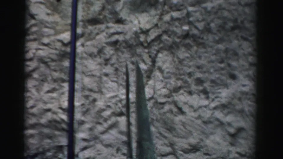Home-movie frame from the Nevada facility showing a tall green structure beside pole supports and a rough rock surface.