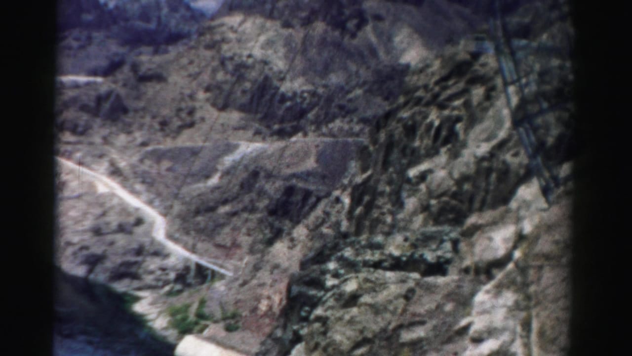 1957 Nevada home-movie view across a rocky canyon, with a winding road and reservoir edge below.