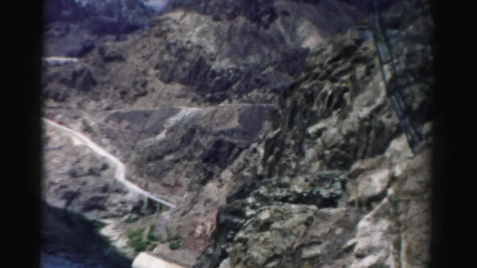 1957 Nevada home-movie view across a rocky canyon, with a winding road and reservoir edge below.