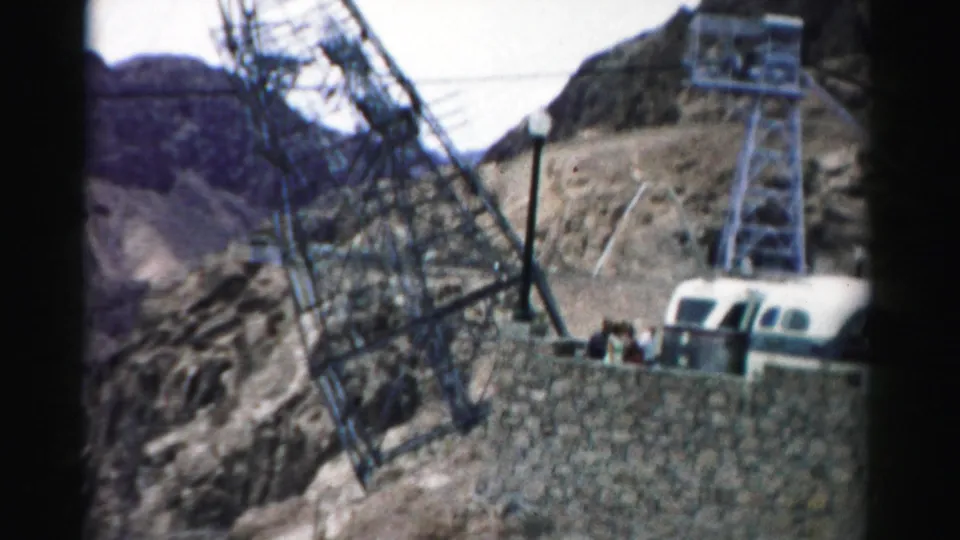 1957 Nevada 8mm frame with lattice power towers, a small vehicle, and tiny visitors near the dam overlook area.